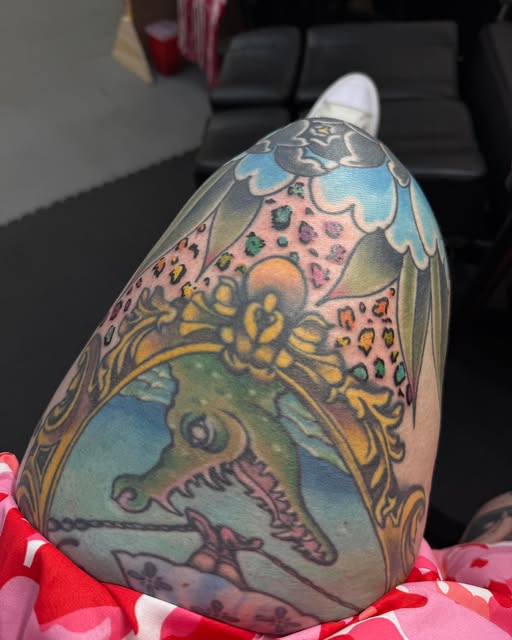 A large colour thigh piece: an ornate gold frame containing a green alligator, with a decorative patterned canopy and scrollwork above it.